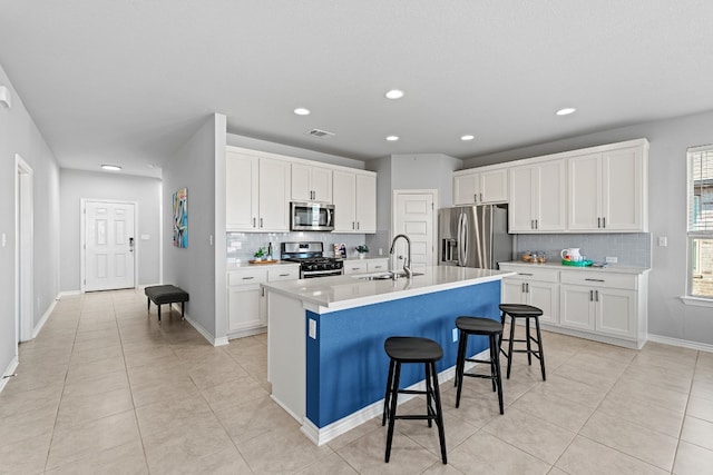 kitchen with a kitchen bar, stainless steel appliances, a kitchen island with sink, sink, and white cabinetry