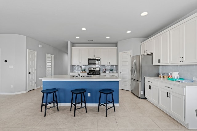 kitchen with white cabinets, a breakfast bar, stainless steel appliances, and an island with sink