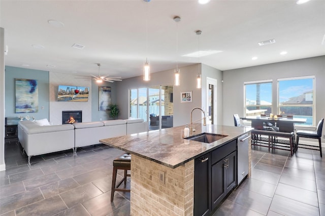 kitchen with sink, a center island with sink, dishwasher, hanging light fixtures, and a breakfast bar area