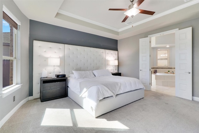 bedroom with ceiling fan, a raised ceiling, light carpet, and ensuite bath