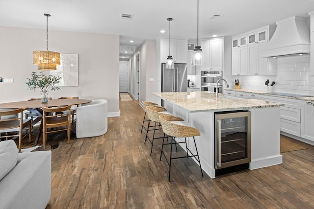 kitchen featuring custom range hood, dark hardwood / wood-style floors, wine cooler, and an island with sink