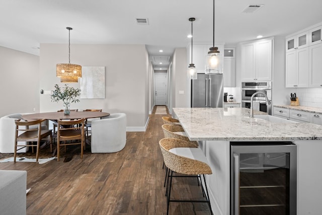 kitchen featuring pendant lighting, dark wood-type flooring, an island with sink, appliances with stainless steel finishes, and beverage cooler