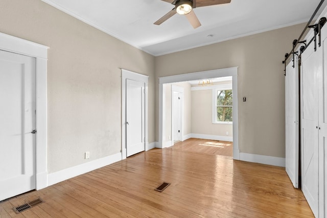 unfurnished bedroom featuring ceiling fan, crown molding, a barn door, and light hardwood / wood-style flooring