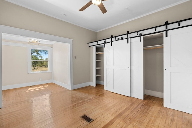 unfurnished bedroom with ceiling fan, light wood-type flooring, ornamental molding, and a barn door