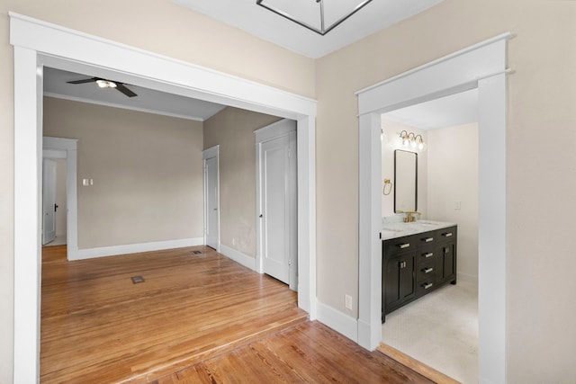 corridor featuring sink, light wood-type flooring, and crown molding