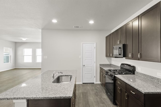 kitchen with visible vents, a center island with sink, a sink, light stone counters, and black range with gas stovetop