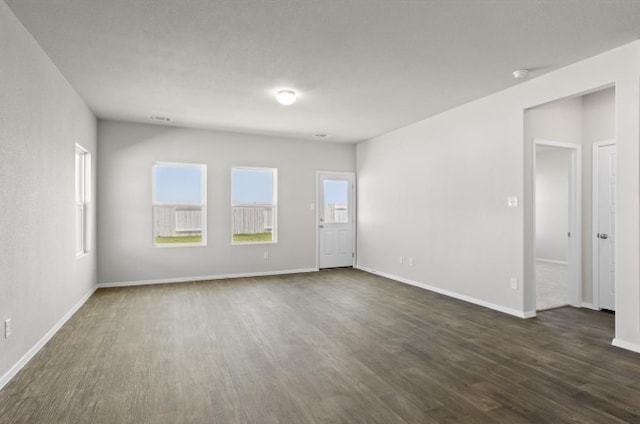 spare room featuring dark wood finished floors, a healthy amount of sunlight, and baseboards