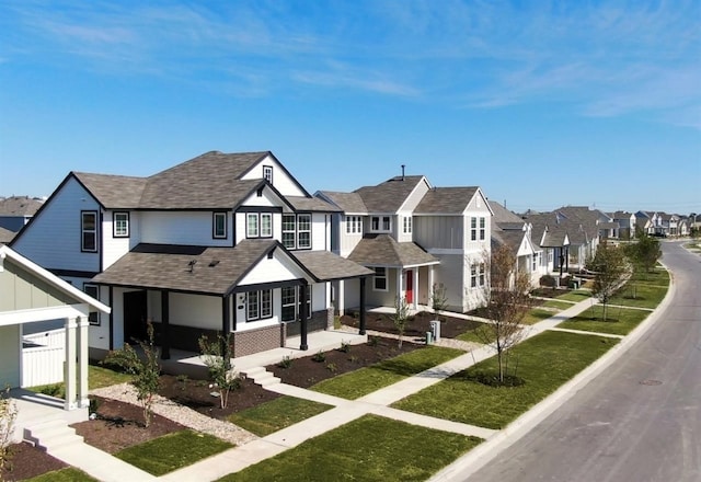 view of front of property featuring covered porch, a residential view, a shingled roof, a front lawn, and brick siding