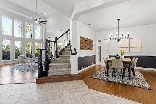 dining room featuring ceiling fan with notable chandelier, light wood-type flooring, ornamental molding, and a high ceiling