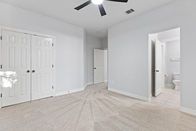 unfurnished bedroom with a closet, light colored carpet, ensuite bath, and ceiling fan