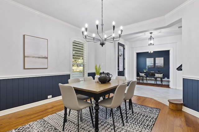 dining space with wood-type flooring, ornamental molding, and a notable chandelier