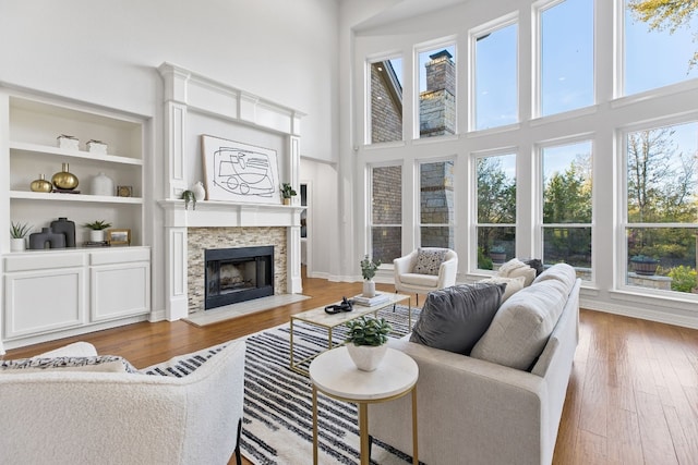 living room with a stone fireplace, built in features, hardwood / wood-style floors, and a high ceiling