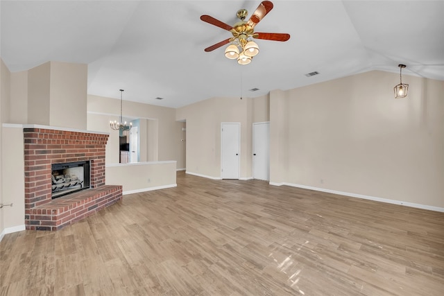 unfurnished living room with ceiling fan with notable chandelier, light wood-type flooring, a brick fireplace, and vaulted ceiling