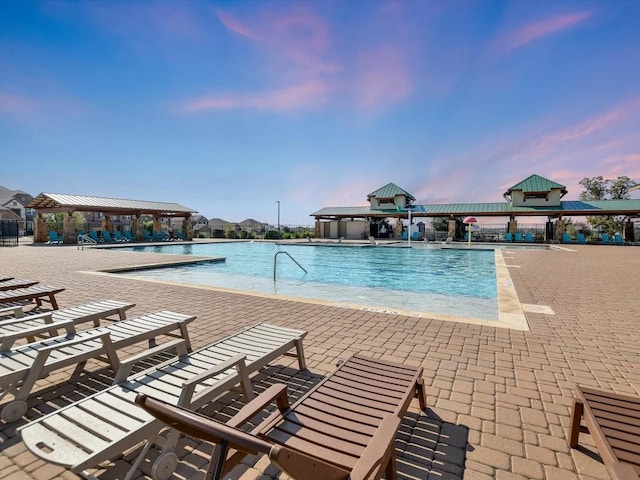 pool at dusk with a patio area, a gazebo, and a community pool