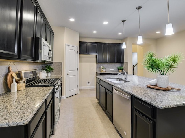 kitchen with stainless steel appliances, hanging light fixtures, a sink, and dark cabinets