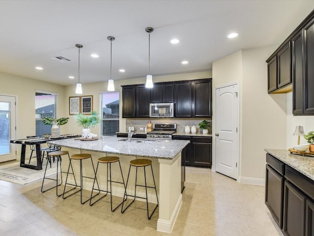 kitchen featuring appliances with stainless steel finishes, a kitchen breakfast bar, light stone countertops, and visible vents