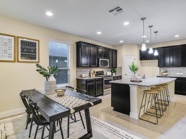 kitchen with a center island, decorative backsplash, appliances with stainless steel finishes, decorative light fixtures, and light stone counters