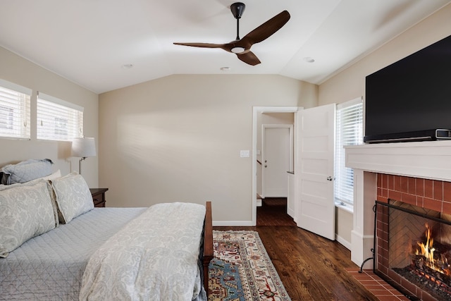 bedroom with ceiling fan, dark hardwood / wood-style flooring, a tile fireplace, and vaulted ceiling