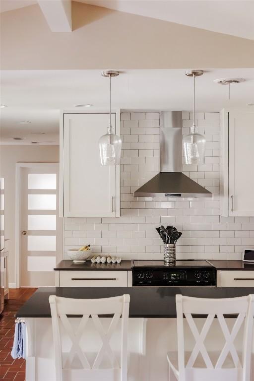 kitchen with decorative backsplash, pendant lighting, vaulted ceiling, and wall chimney exhaust hood