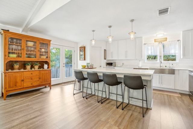 kitchen with white cabinetry, a center island, light hardwood / wood-style floors, and decorative light fixtures