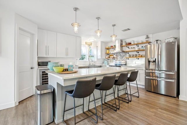 kitchen with a kitchen island, appliances with stainless steel finishes, tasteful backsplash, light hardwood / wood-style floors, and white cabinetry