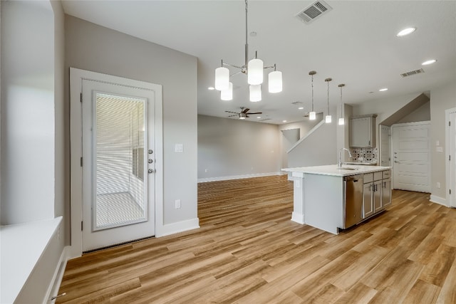 kitchen with gray cabinets, hanging light fixtures, a kitchen island with sink, and light hardwood / wood-style flooring