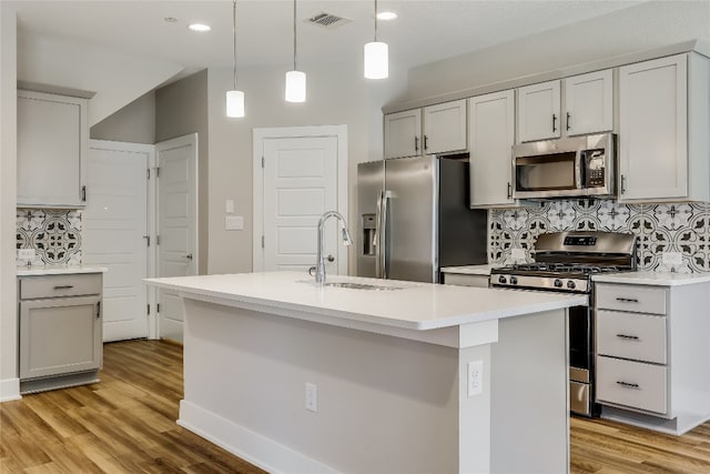 kitchen with tasteful backsplash, stainless steel appliances, a center island with sink, light hardwood / wood-style floors, and hanging light fixtures