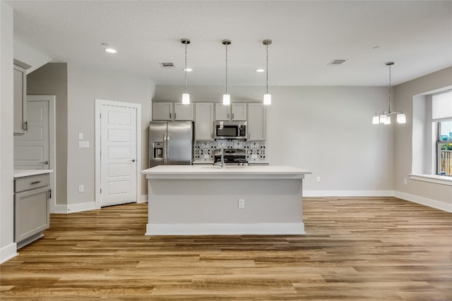 kitchen featuring gray cabinetry, pendant lighting, light wood-type flooring, an island with sink, and appliances with stainless steel finishes