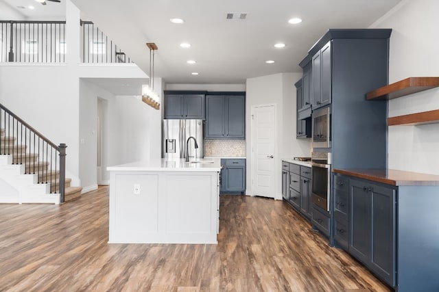 kitchen featuring dark wood-type flooring, blue cabinets, decorative light fixtures, stainless steel appliances, and decorative backsplash