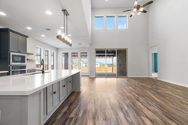 kitchen with built in microwave, dark wood-type flooring, sink, gray cabinetry, and an island with sink