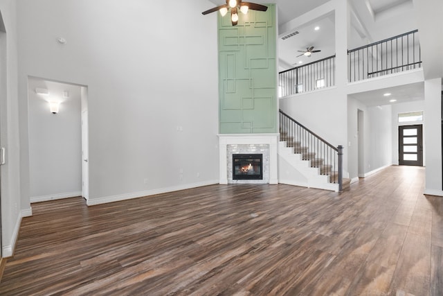 unfurnished living room featuring a tiled fireplace, ceiling fan, a towering ceiling, and dark hardwood / wood-style flooring