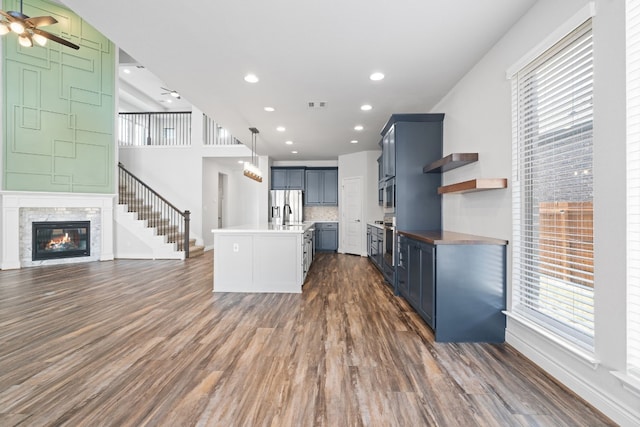 kitchen with appliances with stainless steel finishes, dark hardwood / wood-style flooring, hanging light fixtures, a kitchen island with sink, and ceiling fan