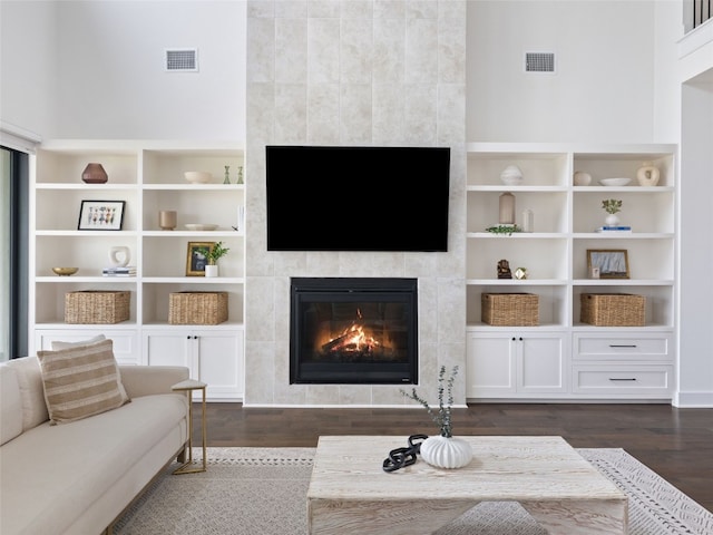 living room featuring dark hardwood / wood-style floors, a towering ceiling, and a tile fireplace