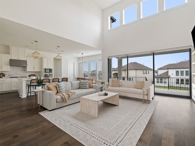 living room with dark hardwood / wood-style flooring, a towering ceiling, and a chandelier