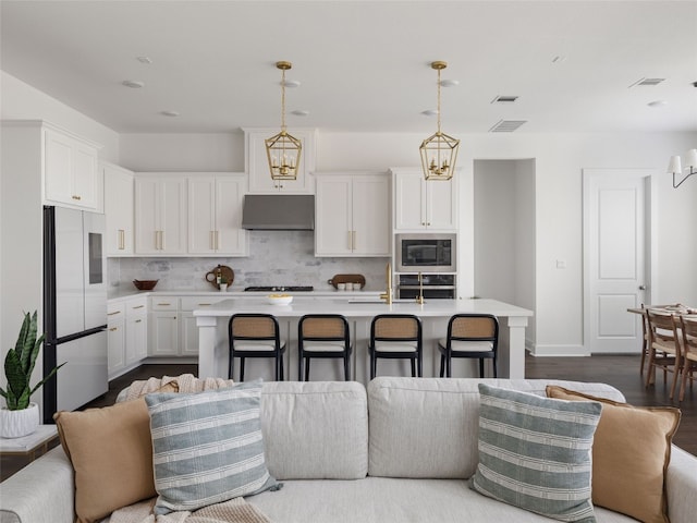 kitchen with white cabinets, pendant lighting, stainless steel appliances, and a kitchen island with sink