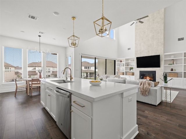 kitchen with white cabinets, stainless steel dishwasher, a kitchen island with sink, sink, and a fireplace