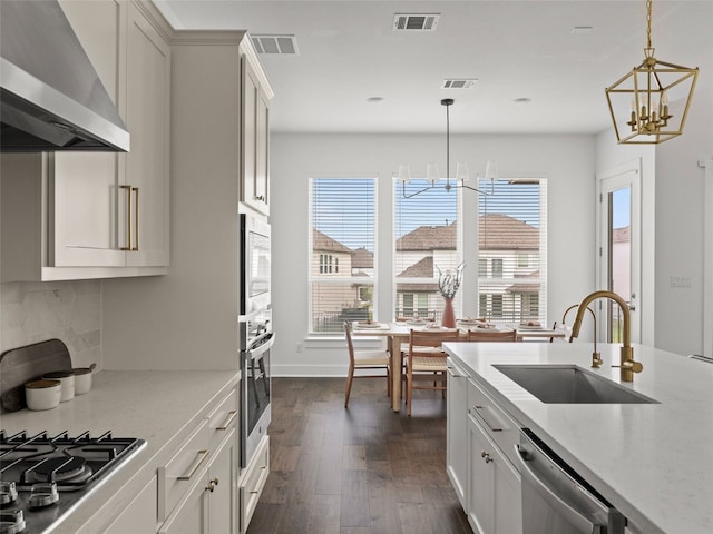 kitchen with sink, hanging light fixtures, wall chimney exhaust hood, stainless steel appliances, and a chandelier