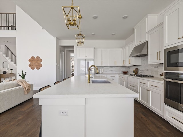 kitchen with decorative light fixtures, sink, a kitchen island with sink, and dark wood-type flooring