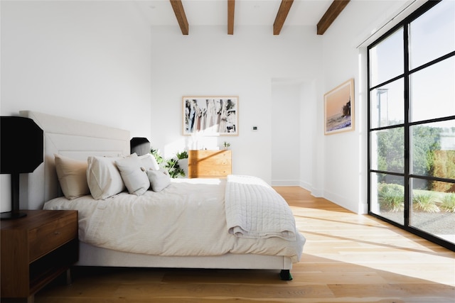 bedroom featuring beamed ceiling, light wood-type flooring, and multiple windows