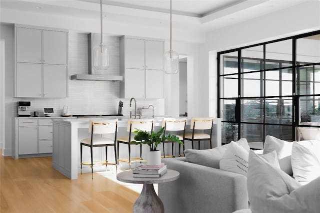 kitchen with a kitchen breakfast bar, hanging light fixtures, light hardwood / wood-style flooring, wall chimney exhaust hood, and tasteful backsplash