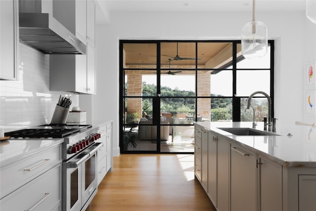 kitchen featuring double oven range, sink, wall chimney exhaust hood, light stone countertops, and light hardwood / wood-style floors