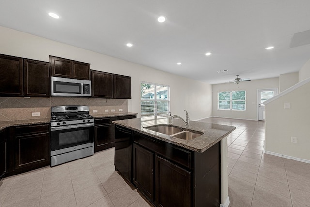 kitchen with sink, light tile patterned floors, appliances with stainless steel finishes, a kitchen island with sink, and backsplash