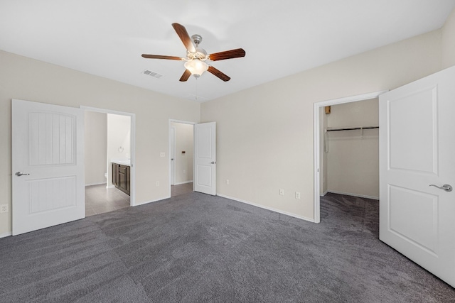 unfurnished bedroom with ensuite bathroom, dark colored carpet, a spacious closet, a closet, and ceiling fan