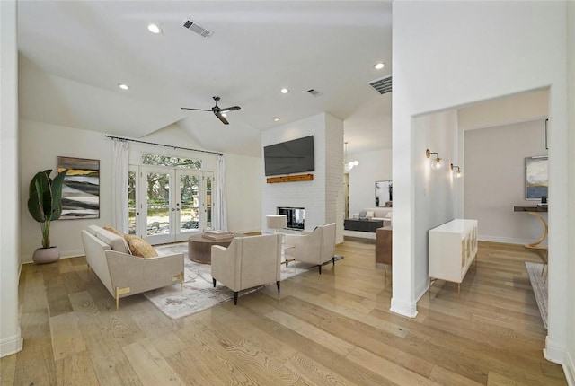 living room featuring french doors, a large fireplace, ceiling fan, light hardwood / wood-style flooring, and lofted ceiling