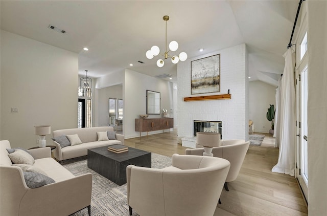 living room with a brick fireplace, light wood-type flooring, a high ceiling, and a chandelier