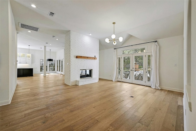 unfurnished living room with french doors, a brick fireplace, a chandelier, lofted ceiling, and light wood-type flooring