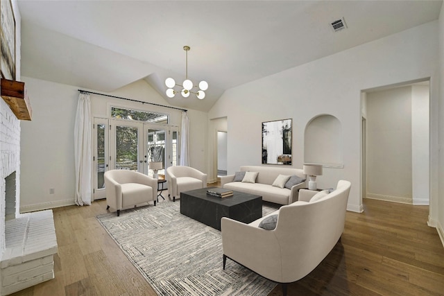 living room with french doors, a fireplace, vaulted ceiling, a chandelier, and light hardwood / wood-style floors