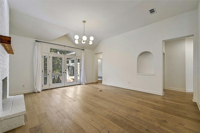 unfurnished living room with french doors, a brick fireplace, a notable chandelier, light hardwood / wood-style floors, and vaulted ceiling