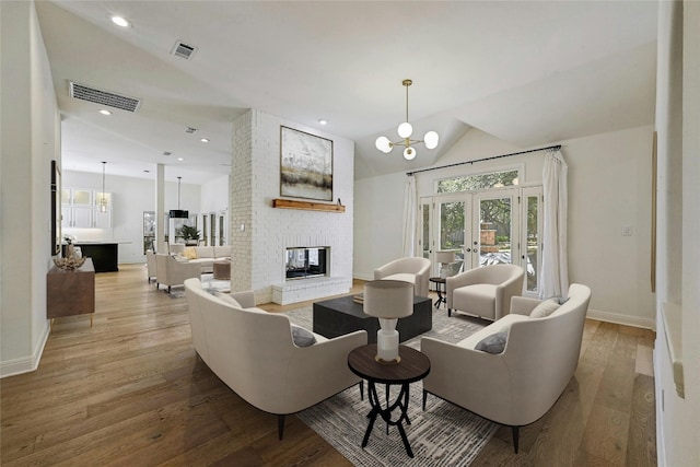 living room featuring french doors, a notable chandelier, a fireplace, hardwood / wood-style floors, and lofted ceiling