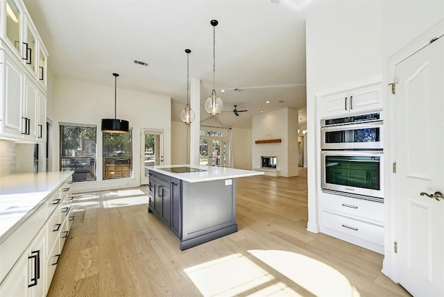 kitchen featuring black electric stovetop, ceiling fan, white cabinets, a center island, and hanging light fixtures